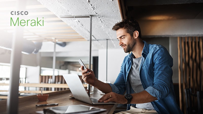 Man working on laptop with phone, Cisco Meraki logo